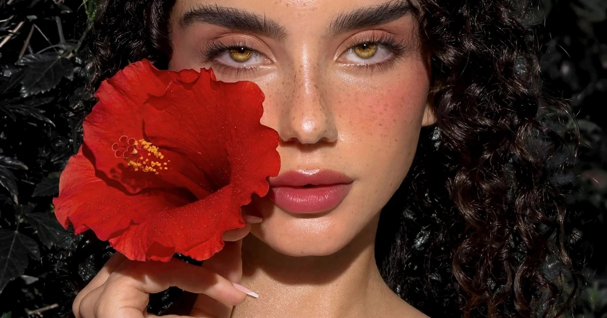 Summer tropical makeup looks with coral eyeshadow, glossy peach lips, and a red hibiscus flower
